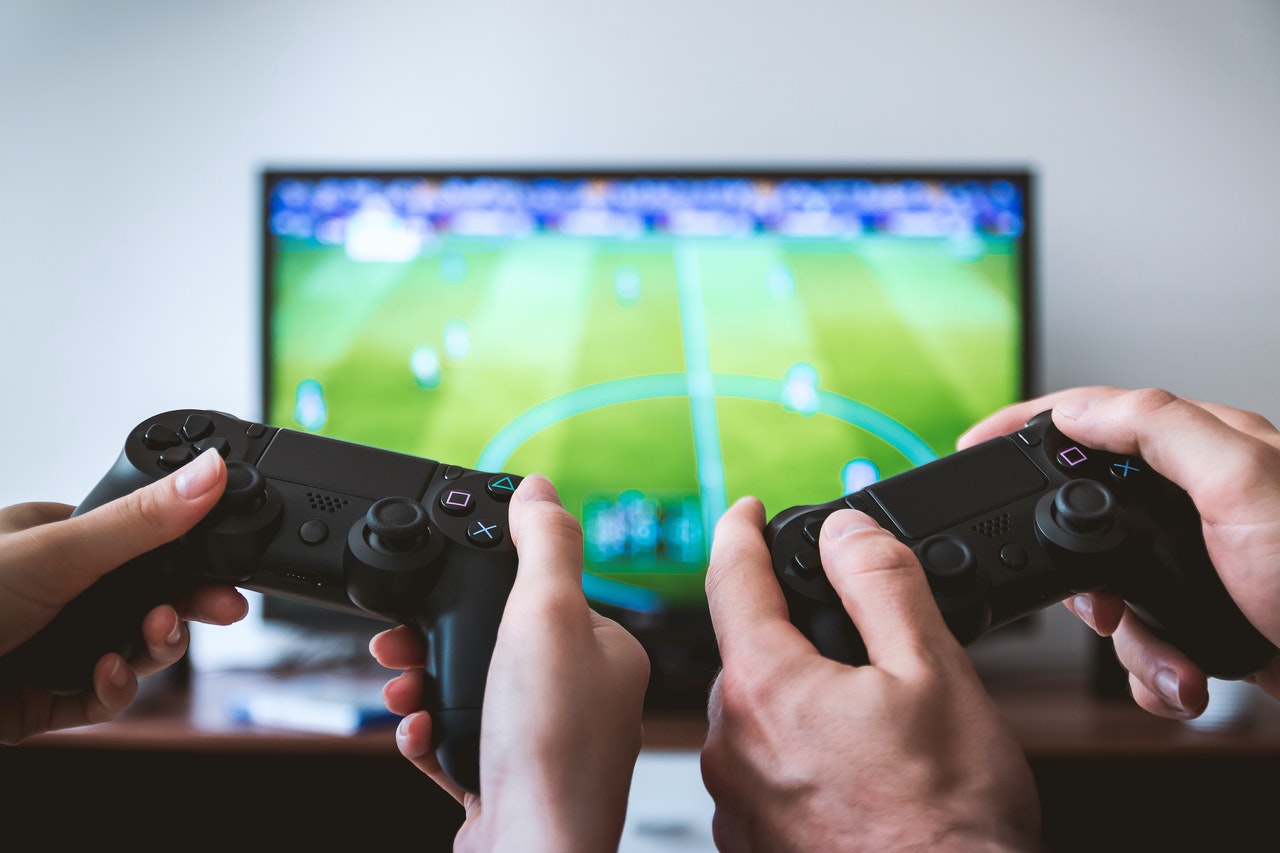 Imagem de duas pessoas segurando seus controles de vídeo game enquanto jogam uma partida de futebol